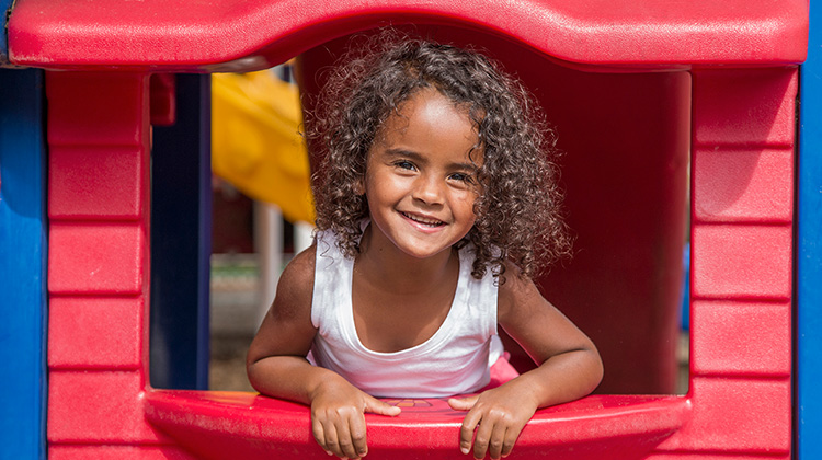 curly haired girl happily leaning out of playhouse