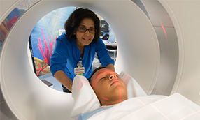 Nurse assisting a young child that is going through an MRI machine.