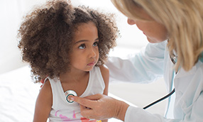 Female doctor placing a stethoscope on young female child to check heart rate.
