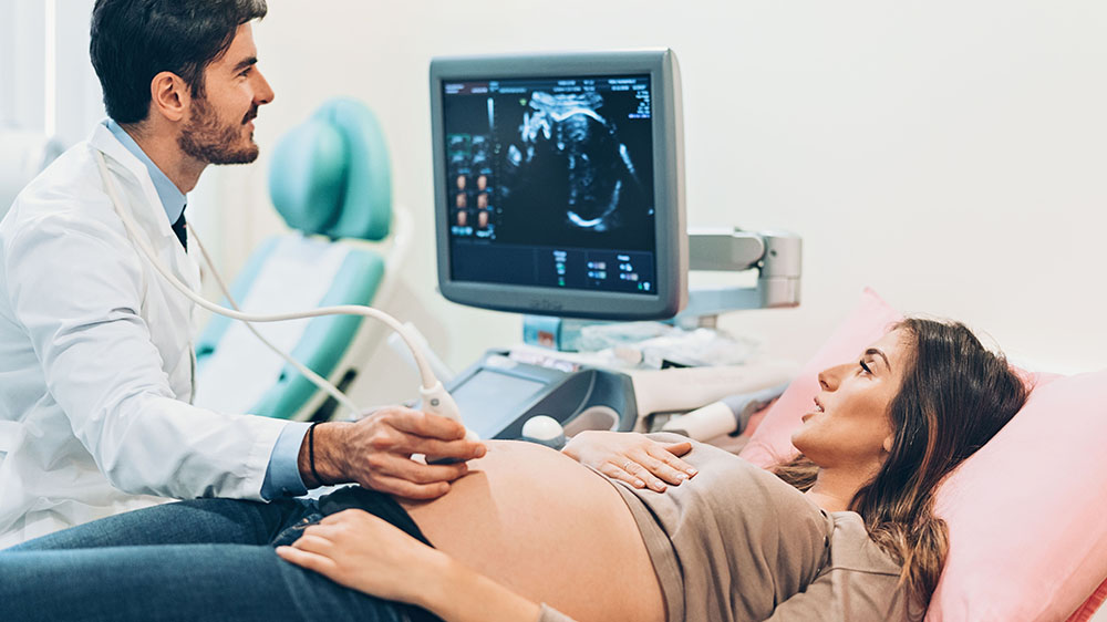 pregnant woman and doctor look at ultrasound screen during exam.