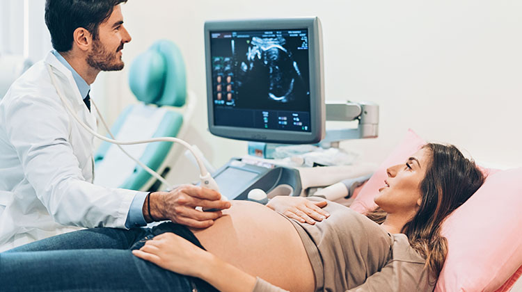 pregnant woman and doctor look at ultrasound screen during exam.