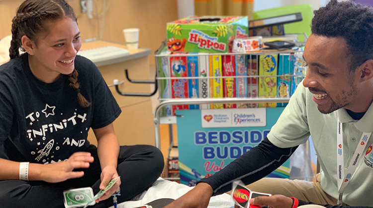 teen volunteer playing a card game with a patient at their bedside.