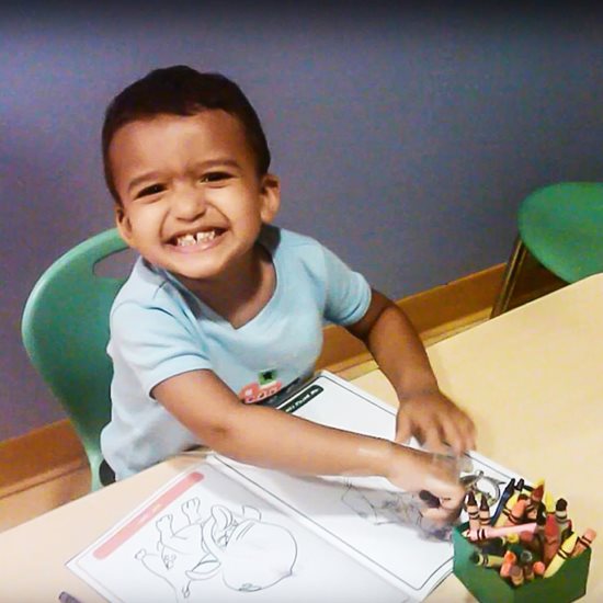 Mateo coloring in a coloring book and smiling at the camera.