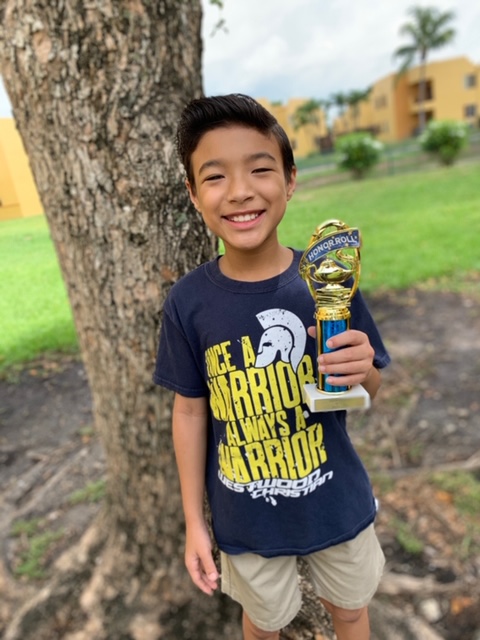 Jayden holding up a trophy in front of a tree. 