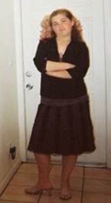 Jennifer de pie frente a una puerta con un vestido oscuro y los brazos cruzados.