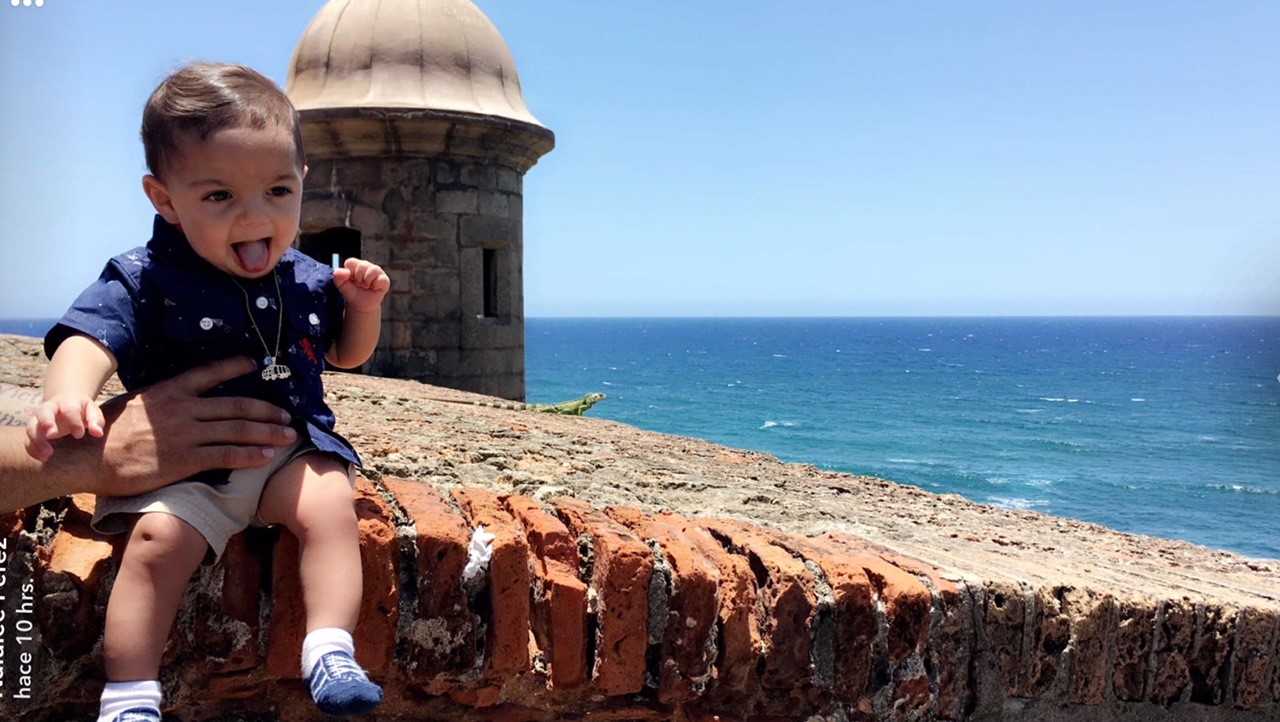 Liam being held up in front of a seaside colonial fort.