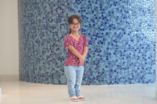 Liz stands in front of a mosaic blue and light blue wall