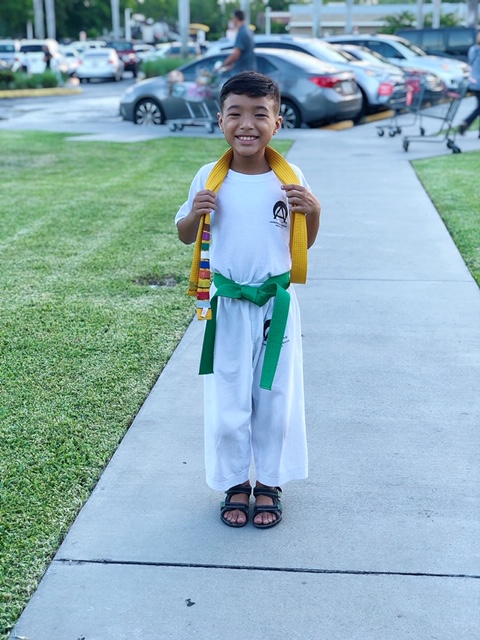 Jayden in his martial arts uniform wearing a green belt and smiling.